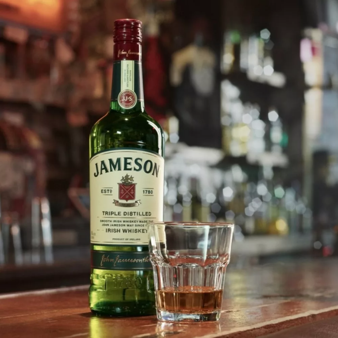 Bottle of Jameson Irish Whiskey with a glass of whiskey on a wooden bar counter in a cozy pub setting