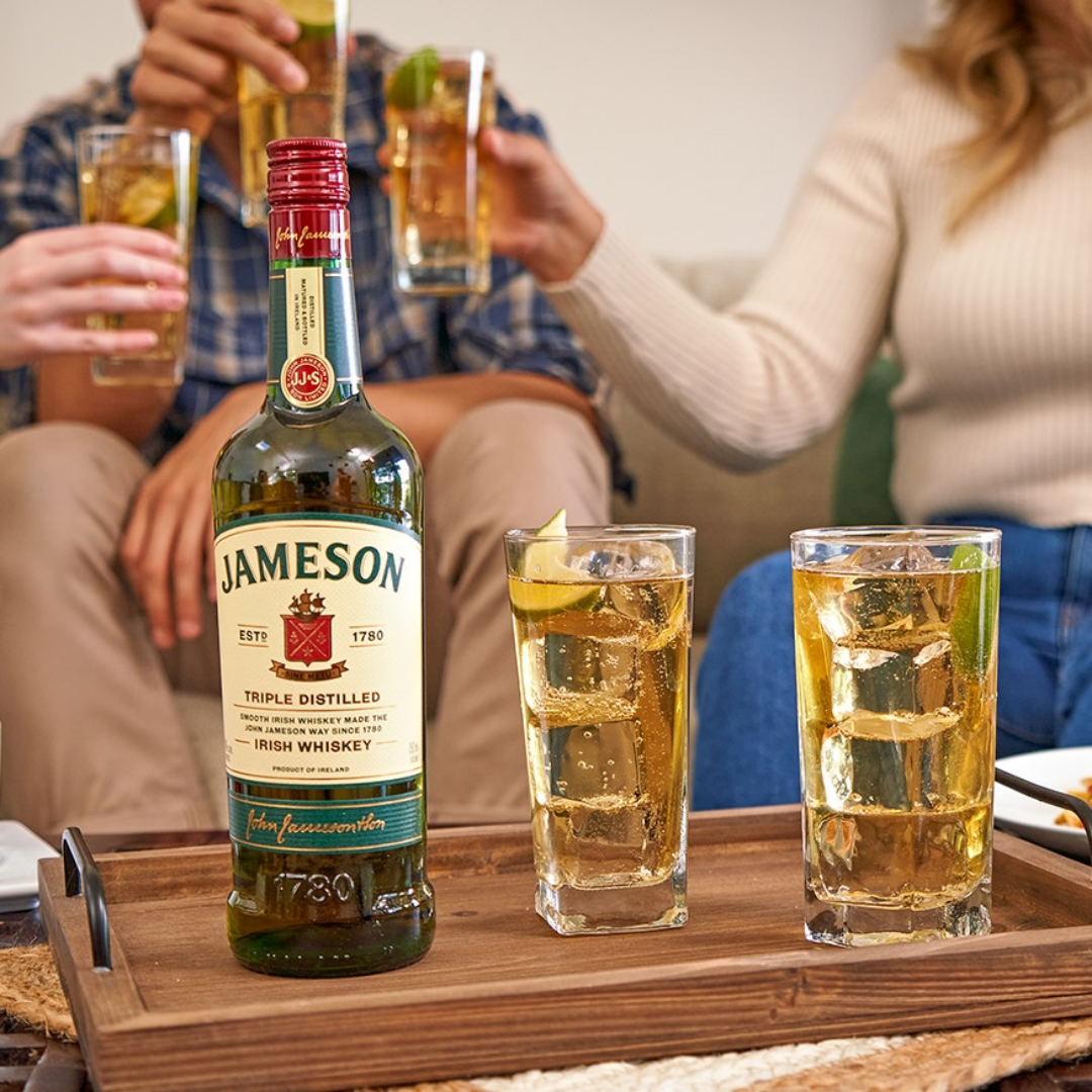 Jameson Irish Whiskey bottle with whiskey highball cocktails and lime on a wooden serving tray during a social gathering