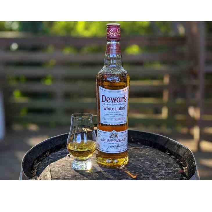 Glass of Dewar’s White Label Scotch whisky served on ice with bottle in background